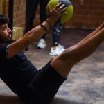 Focused man performing core exercises with a medicine ball in an indoor gym highlighting fitness and strength.